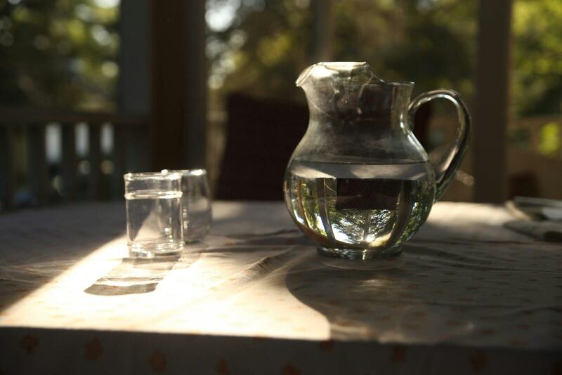 A glass pitcher of water and a drinking glass on a sunlit table