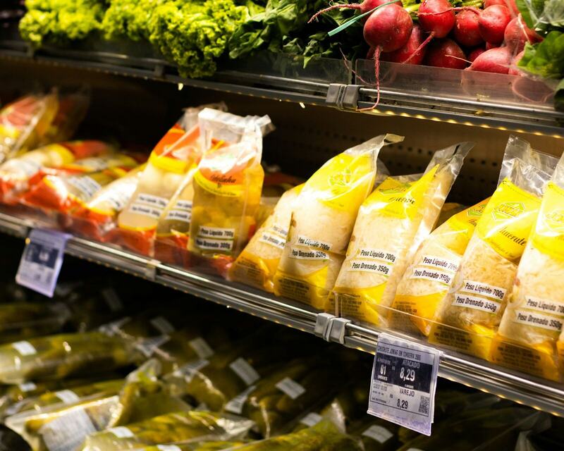 A grocery shelf of greens, radishes and packaged foods with price labels