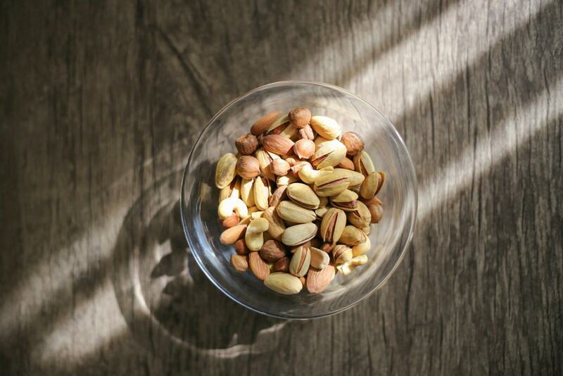 A glass bowl of peanuts on a wooden table in window light