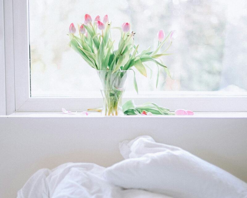Tulips in a glass vase on a windowsill above a white bed