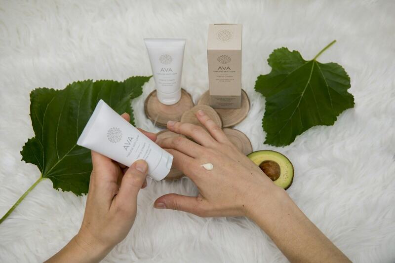 Hands holding a tube of cream beside green leaves
